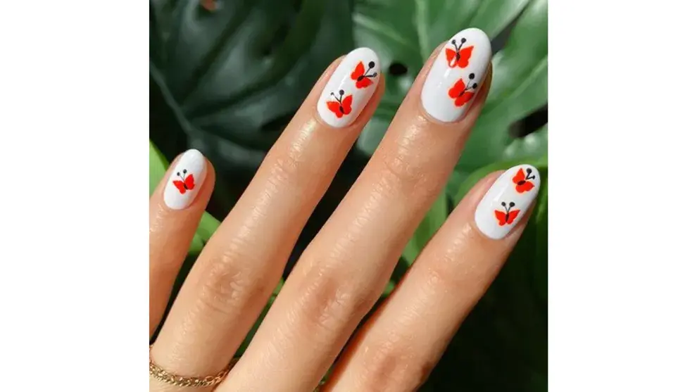 Nail art de mini mariposas naranjas sobre fondo blanco
