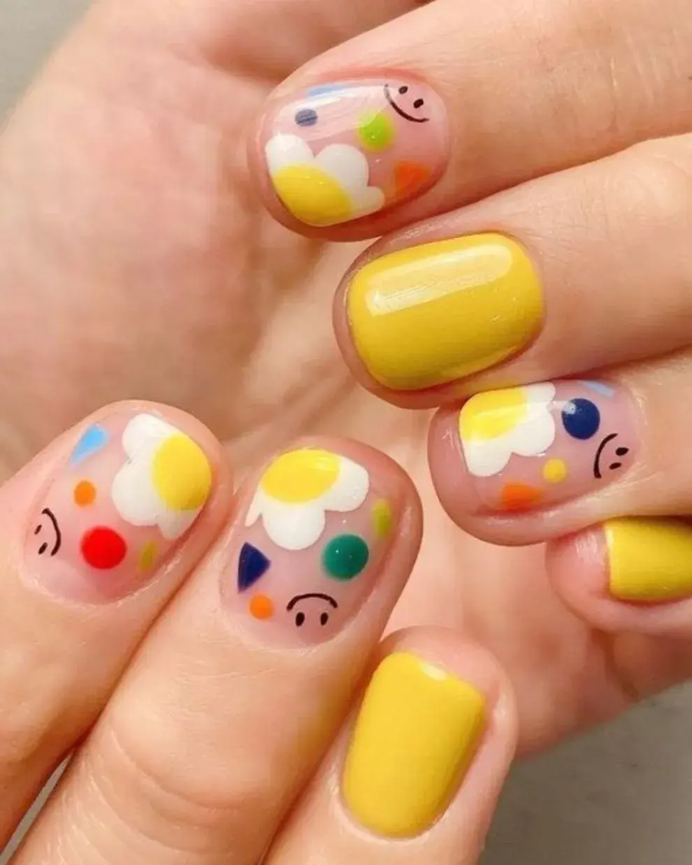 Con uñas en amarillo pleno, en otras diseños cute con flores y caritas felices.