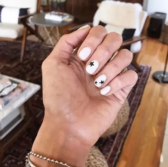 Simple y elegante. Uñas bien cortas y redondeadas, una base blanca o clara y algunas estrellas en esmalte negro.