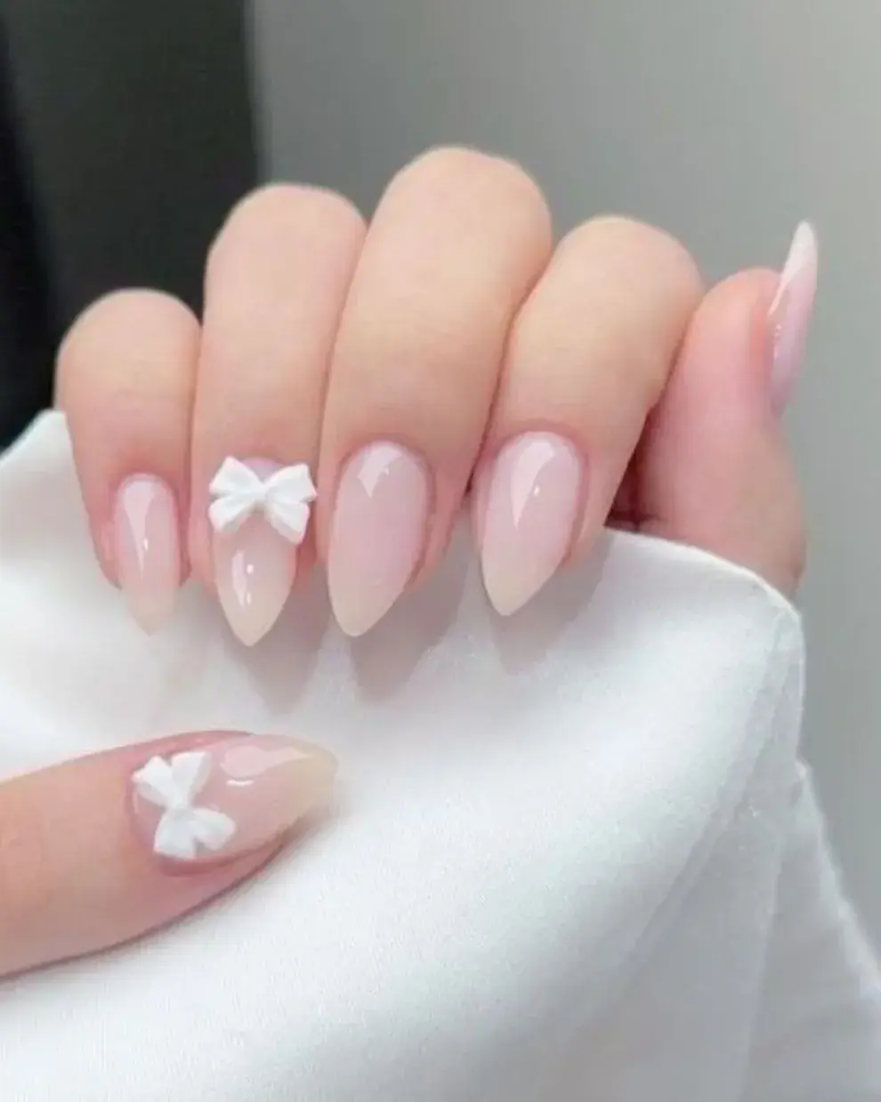 Uñas milky con aplique de moño, muy de la mano de la estética coquette.