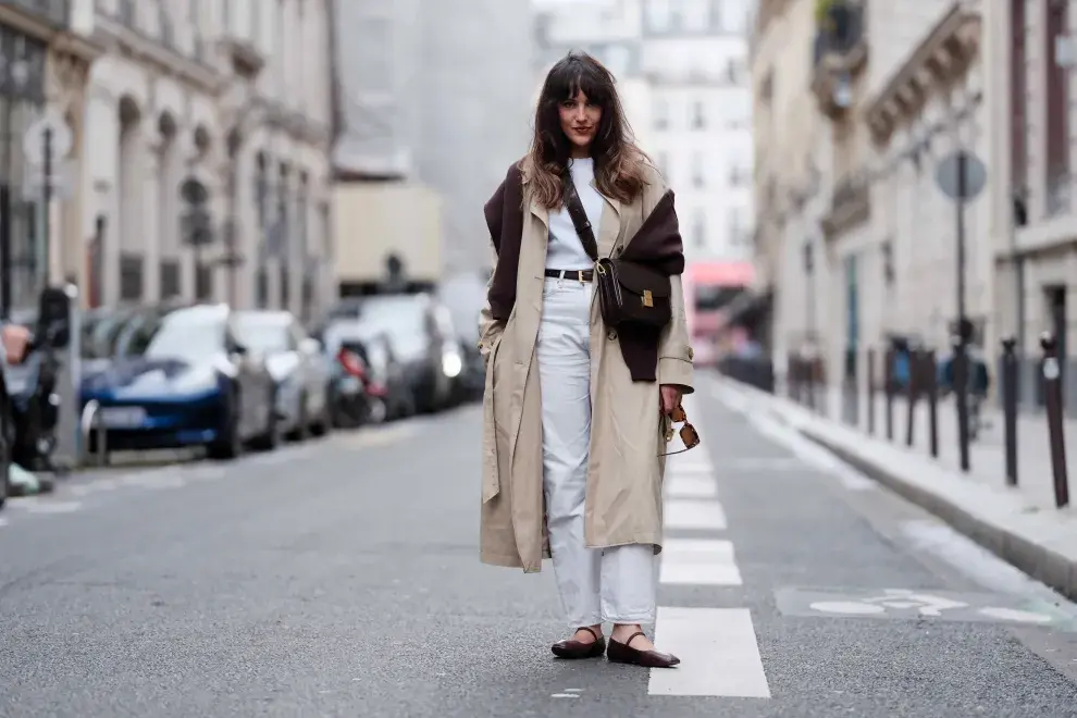 Pantalones blancos, trench y suéter marrón.