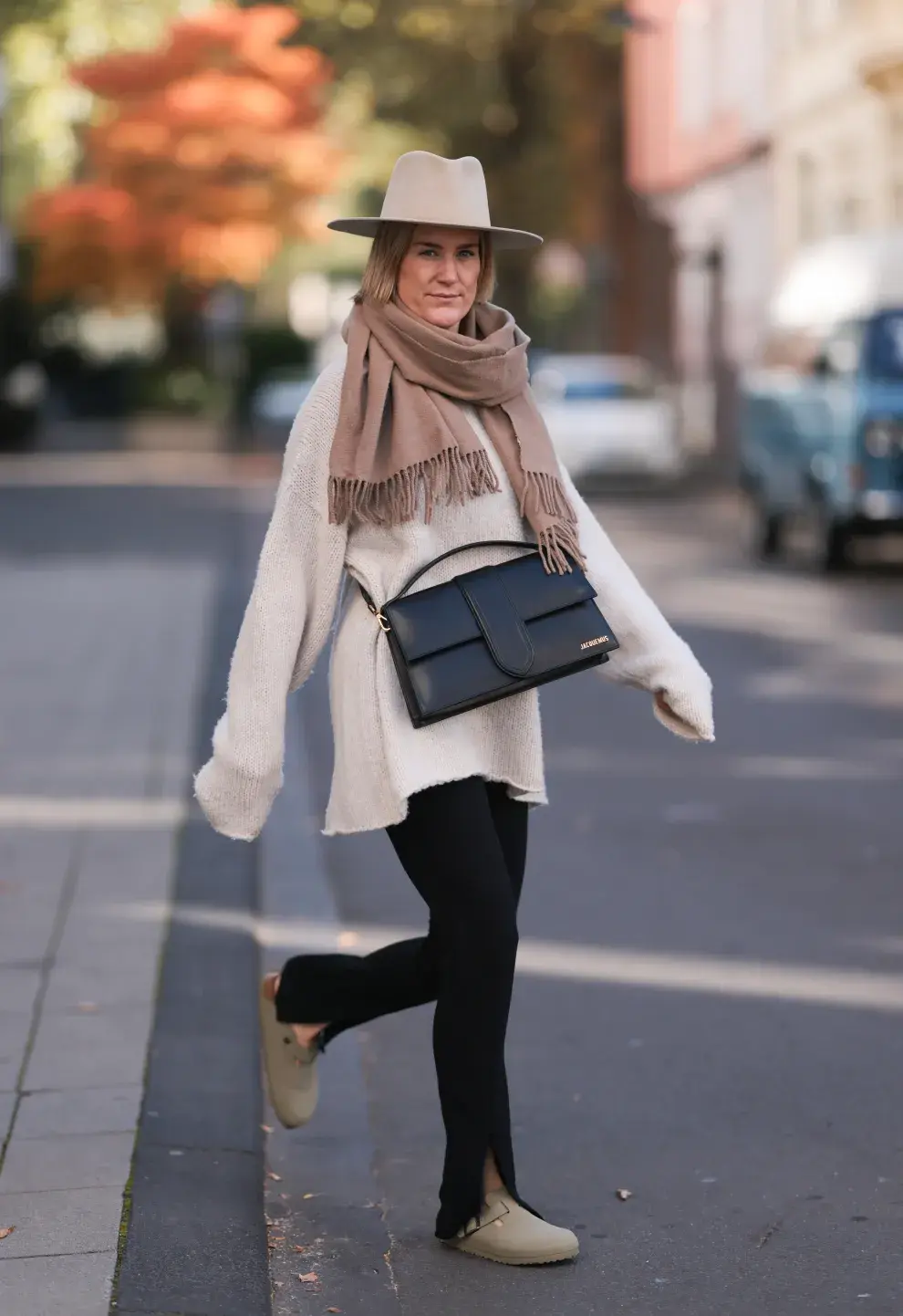 Mujer en la calle con leggins, suéter oversize, maxibufanda y sombrero. 