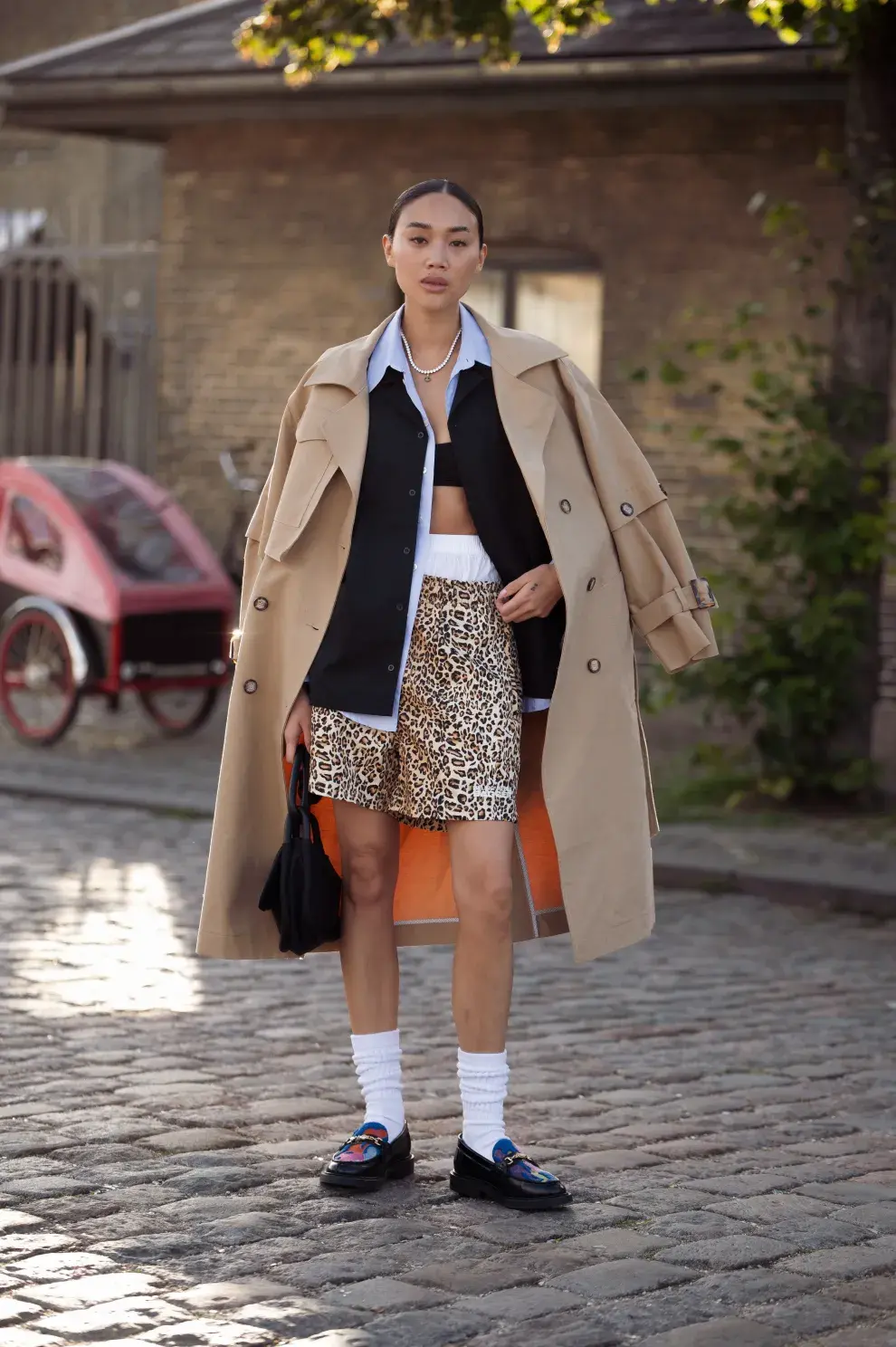 Mujer con bermuda de leopardo y trench en la ciudad.