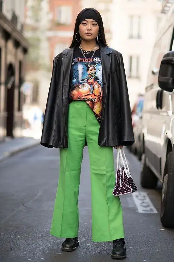 El look incluye un pantalón verde, una remera gráfica y un saco de cuero.