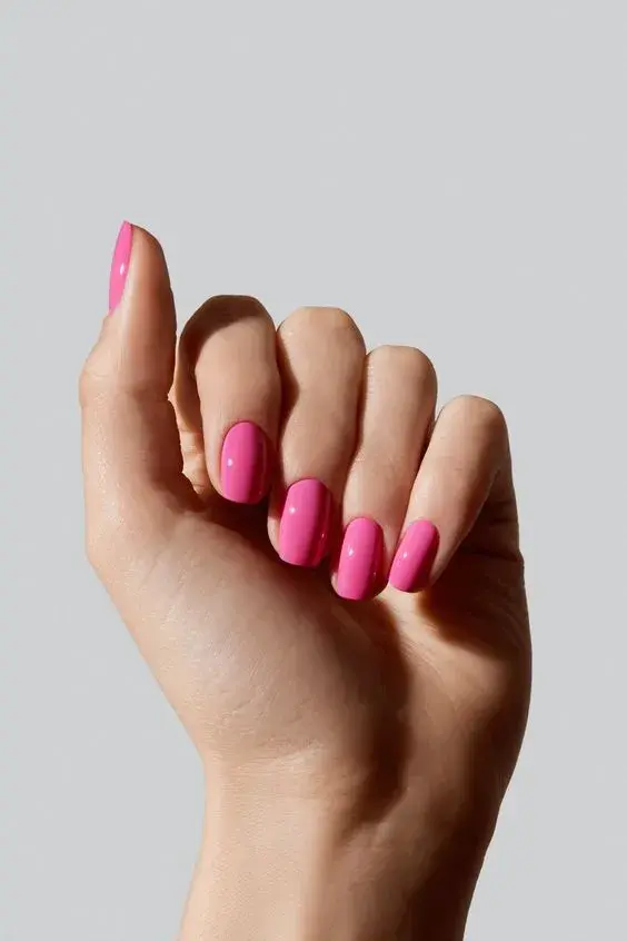 Foto de una mano con esmalte rosa.