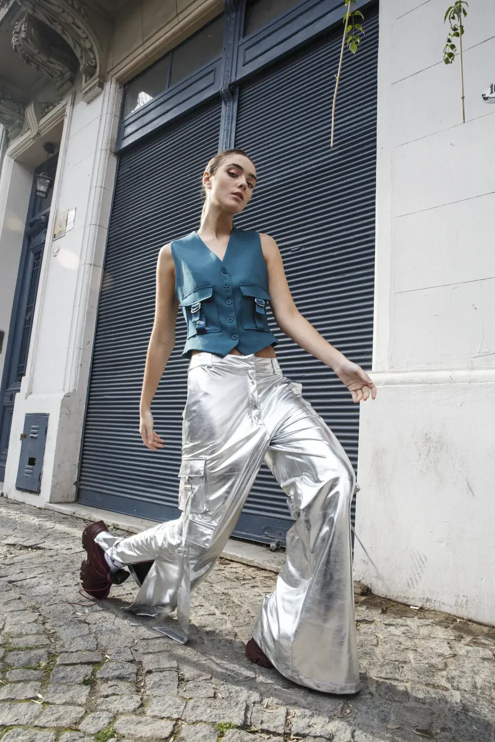 Una mujer caminando por la calle con un pantalón metalizado y un chaleco azul