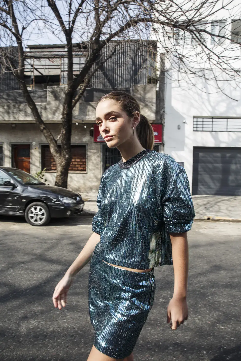 Una mujer caminando con una blusa y una pollera brillante