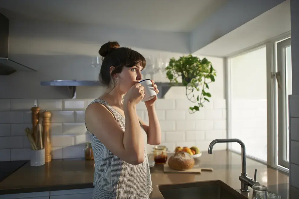 Una mujer tomando una taza de café en la cocina de su casa