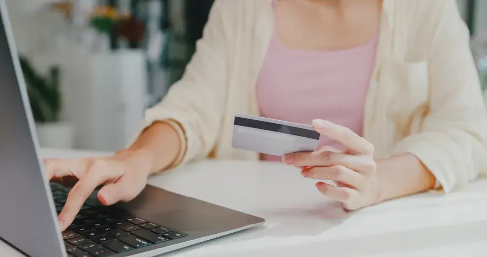 Una mujer haciendo una compra online con una tarjeta de crédito en la mano