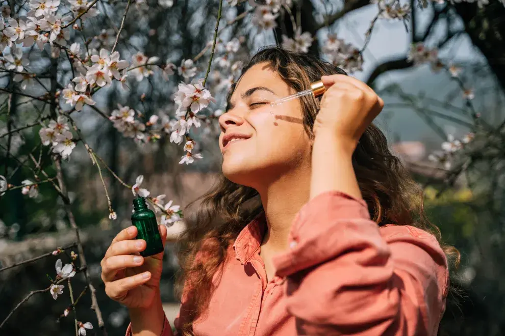 Una mujer poniendose un sérum y flores de fondo