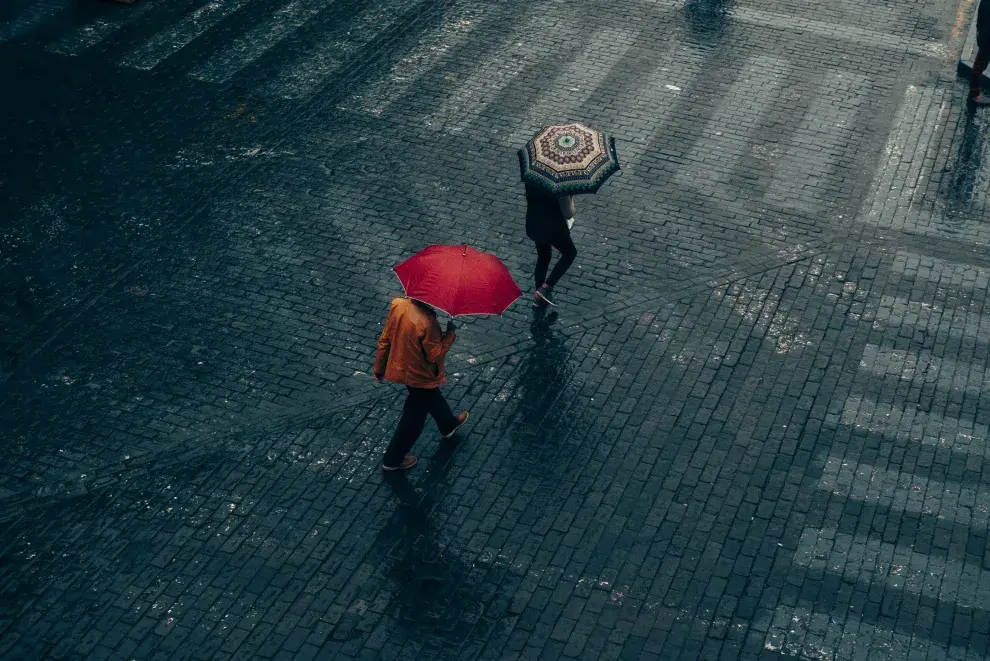 Dos personas debajo de la lluvia caminando con paraguas