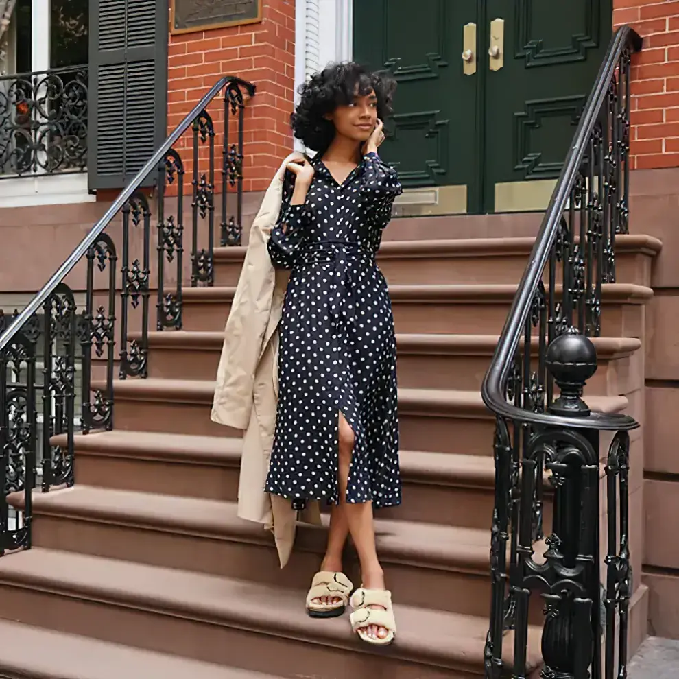 Chica con rulos posando en escalera con un vestido a lunares y sandalias peludas de Birkenstock 