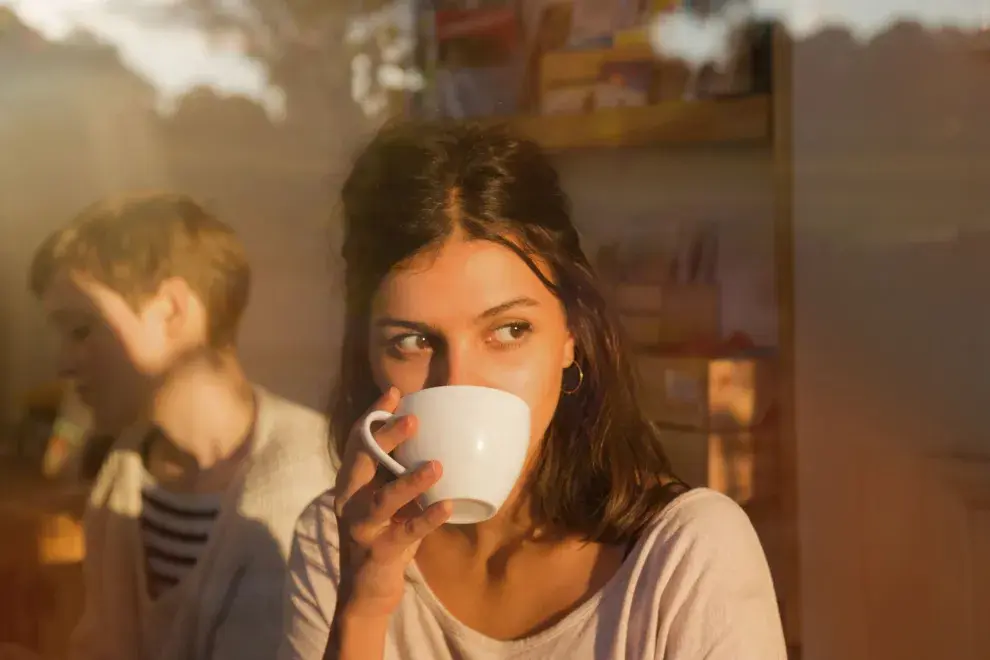 Un mujer tomando una taza de café mirando por la ventana