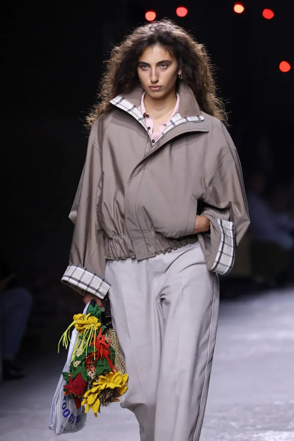 Una mujer desfilando en Milán con un conjunto en color gris y una cartera de flores