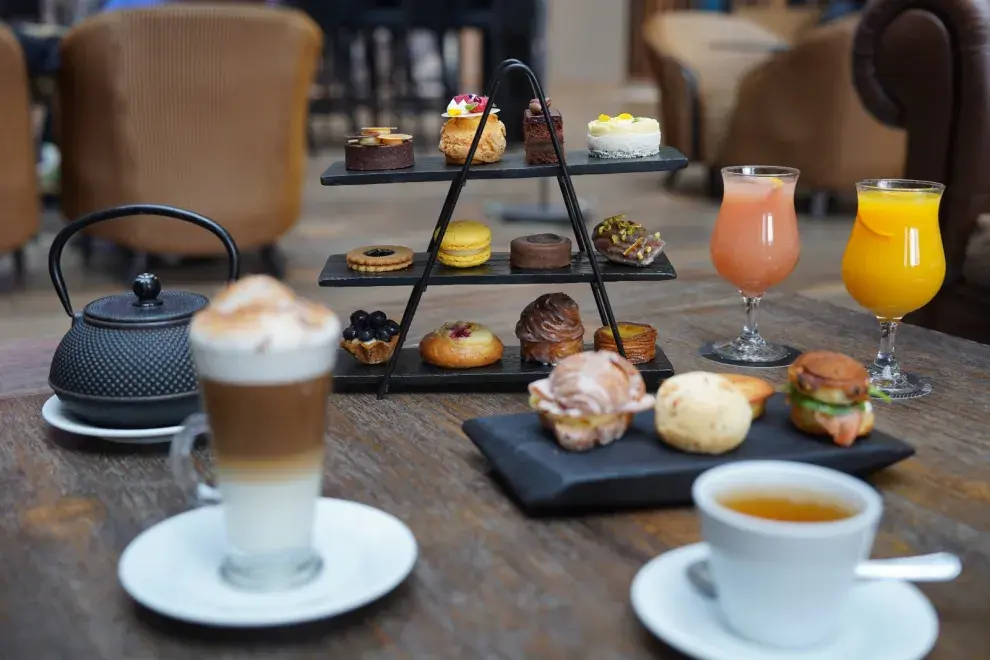 Una mesa servida con una merienda, con cafés y varios dulces de pastelería.