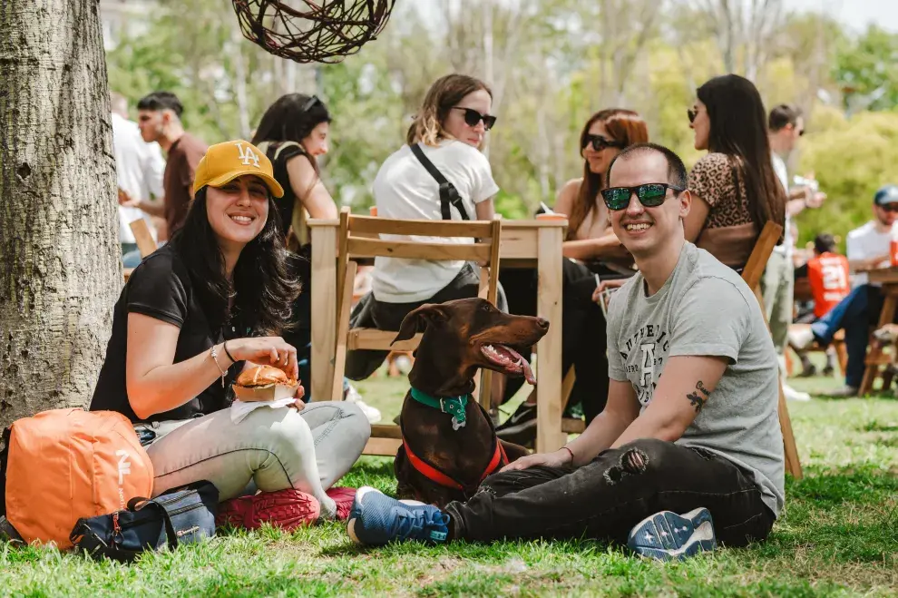 Chica y chico sentados en el pasto en un picnic, con un perrito.