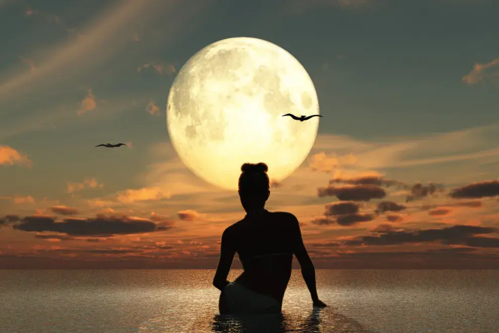 Una mujer mirando una Luna Llena desde el agua.