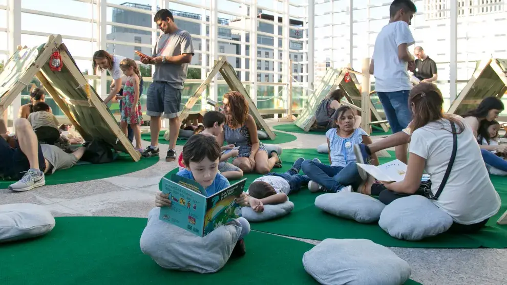 Niños leyendo libros en un parque con libros gigantes en el centro cultural de la ciencia