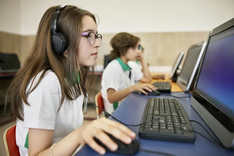 alumna y alumno en escuela usando computadora