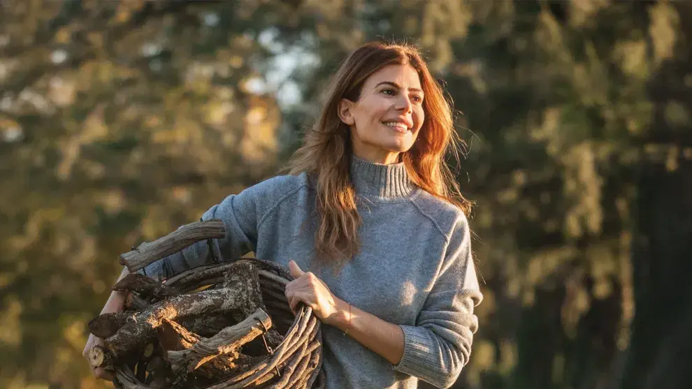 Juliana Awada lleva un sueter gris y un canasto con troncos de madera en el campo