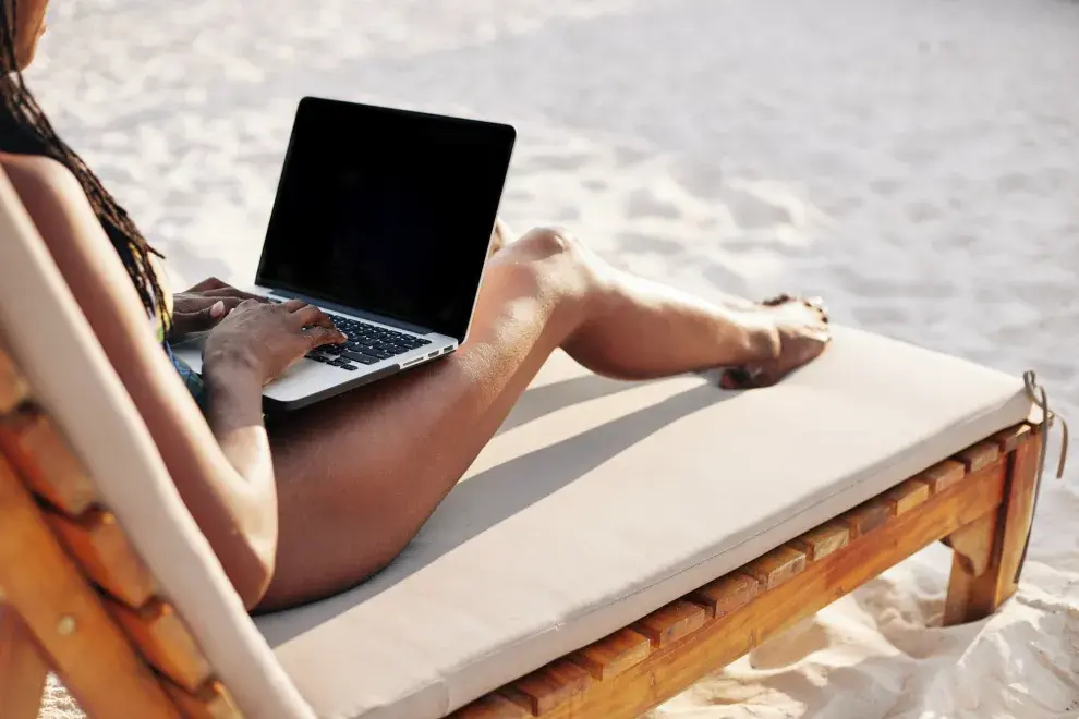 Una mujer en la playa con una laptop sobre las piernas.