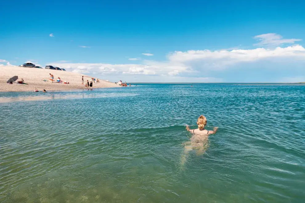 Fotografía de una chica nadando en un mar cristalino y de lejos se ve la arena blanca con un par de personas