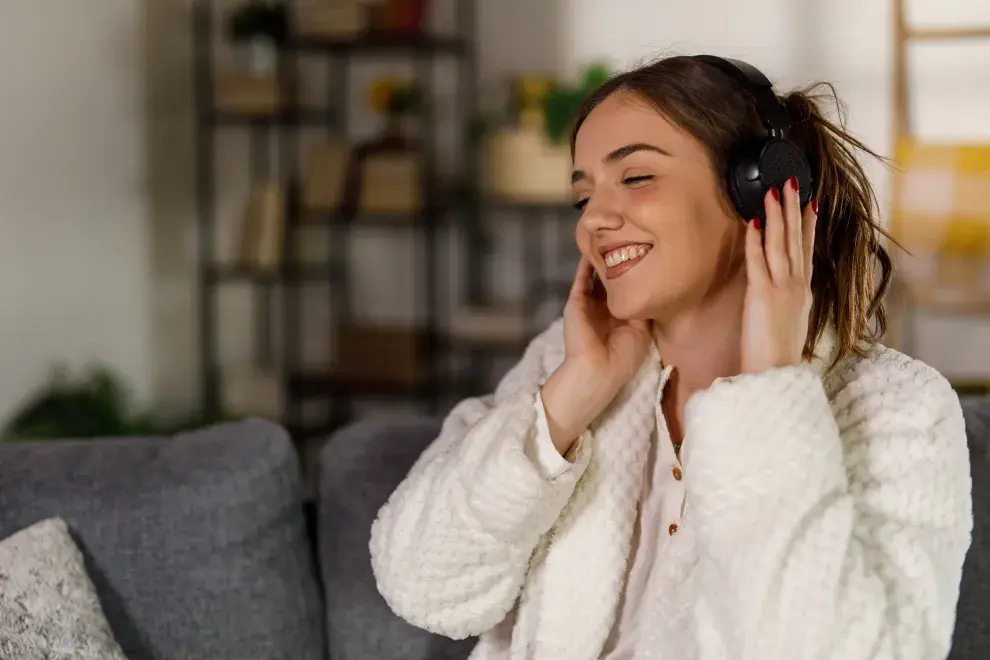 Una mujer escuchando musica desde sus auriculares en el sillón de su casa