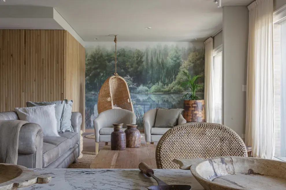 Mural de Sofía Willemoës. Sillón Chesterfield de cuero gris, sillones en lino, alfombra de yute, mesas bajas, objetos de teca de la India y maceta con palmera de Indonesia (todo de Compañía Nativa).