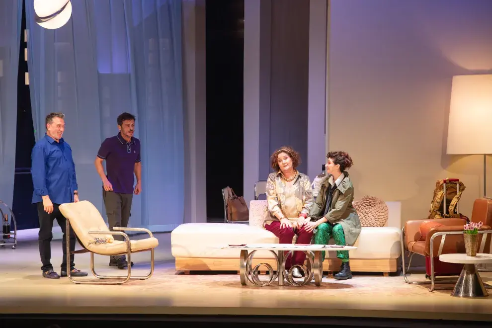 Unas personas sentadas en el living sobre un escenario teatral.