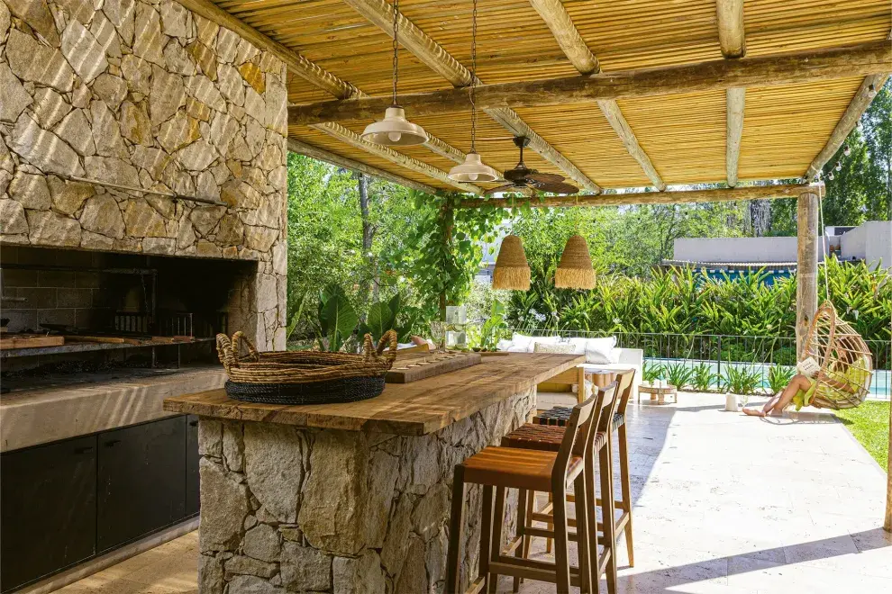 Parrilla y barra con revestimiento de piedra voladura ‘Mar del Plata’ (90% blanca, 10% ocre). Para la pérgola, listones de pino sobre postes y vigas de eucalipto (ART Arquitectos). 