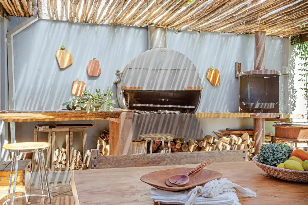 Mesa de tronco de cedro azul, una mesada y barra en lenga, parrilla/horno de chapa y fogonero (Javier Zaldívar). El mantel de tussor es de Lado Blanco Home.