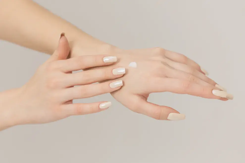 Mujer aplicándose crema en las manos.