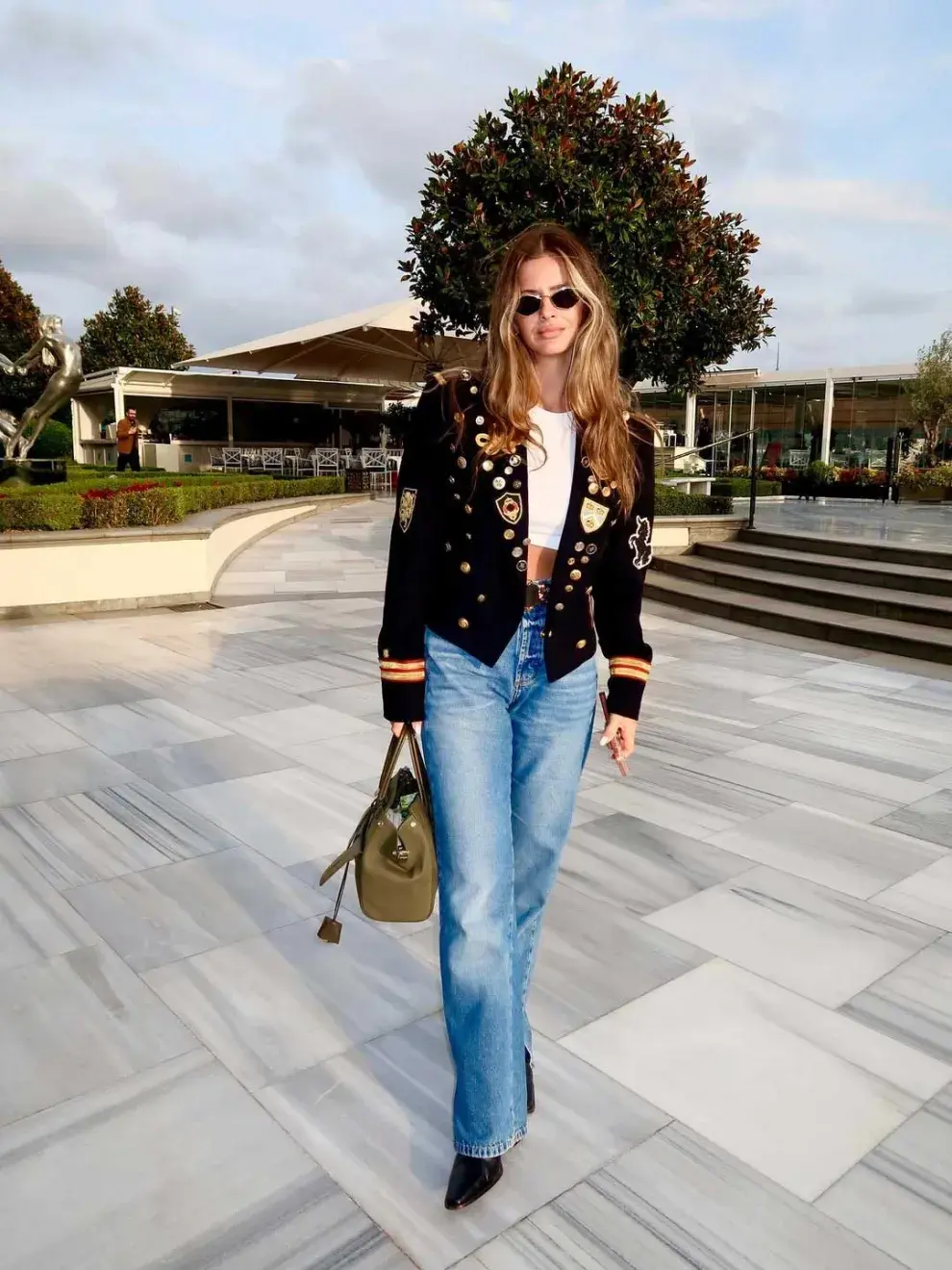 La China apostó por un conjunto que grita elegancia urbana: jeans anchos, remera blanca cropped y un cinturón marrón con hebilla XL que enmarca la silueta con carácter.