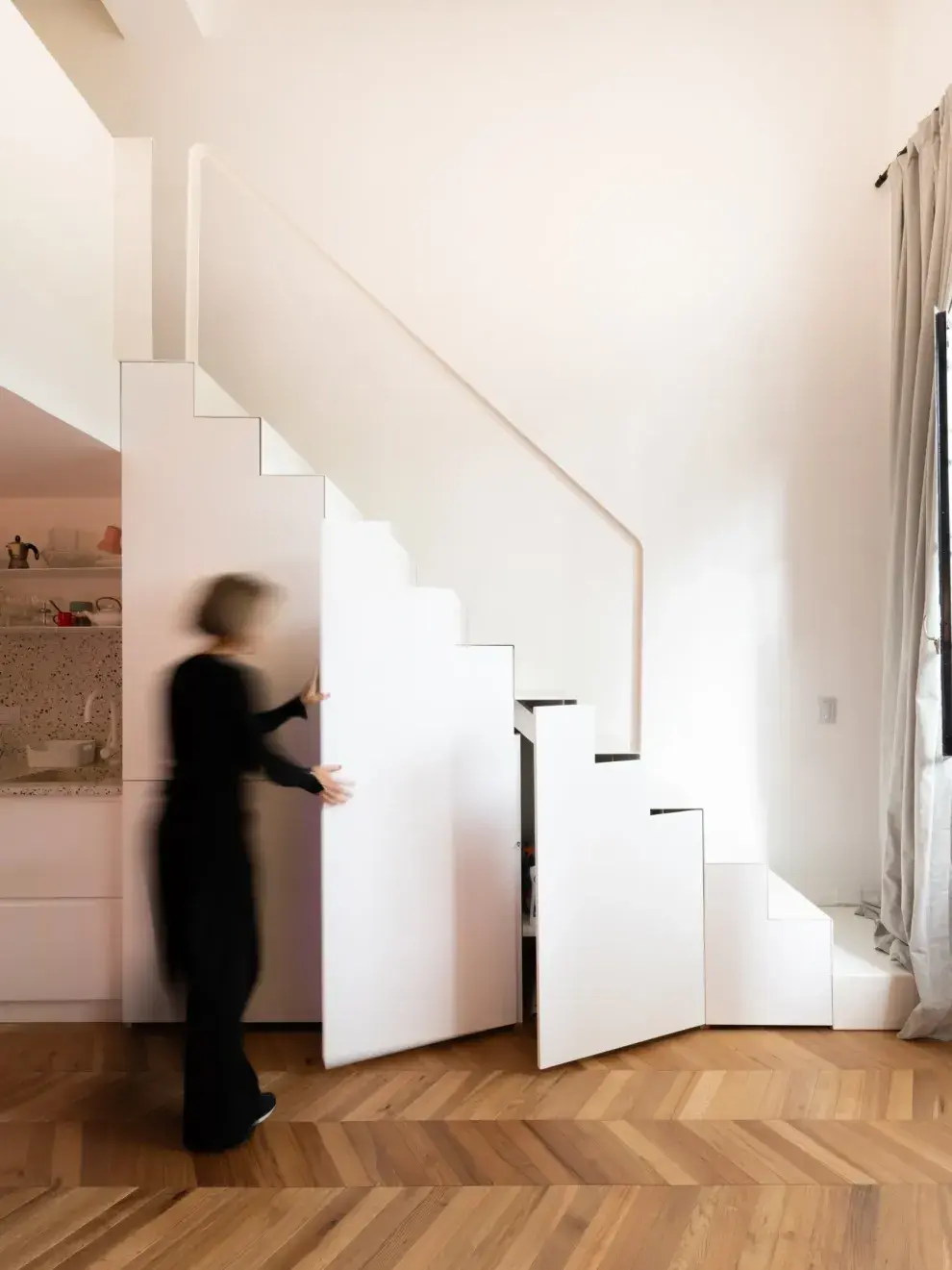 El secreto estuvo en trasladar la cocina al nivel inferior e integrarla al ambiente principal con un diseño minimalista fundido en una sola pieza de metal plegado que también funciona como armario, despensa y heladera. 