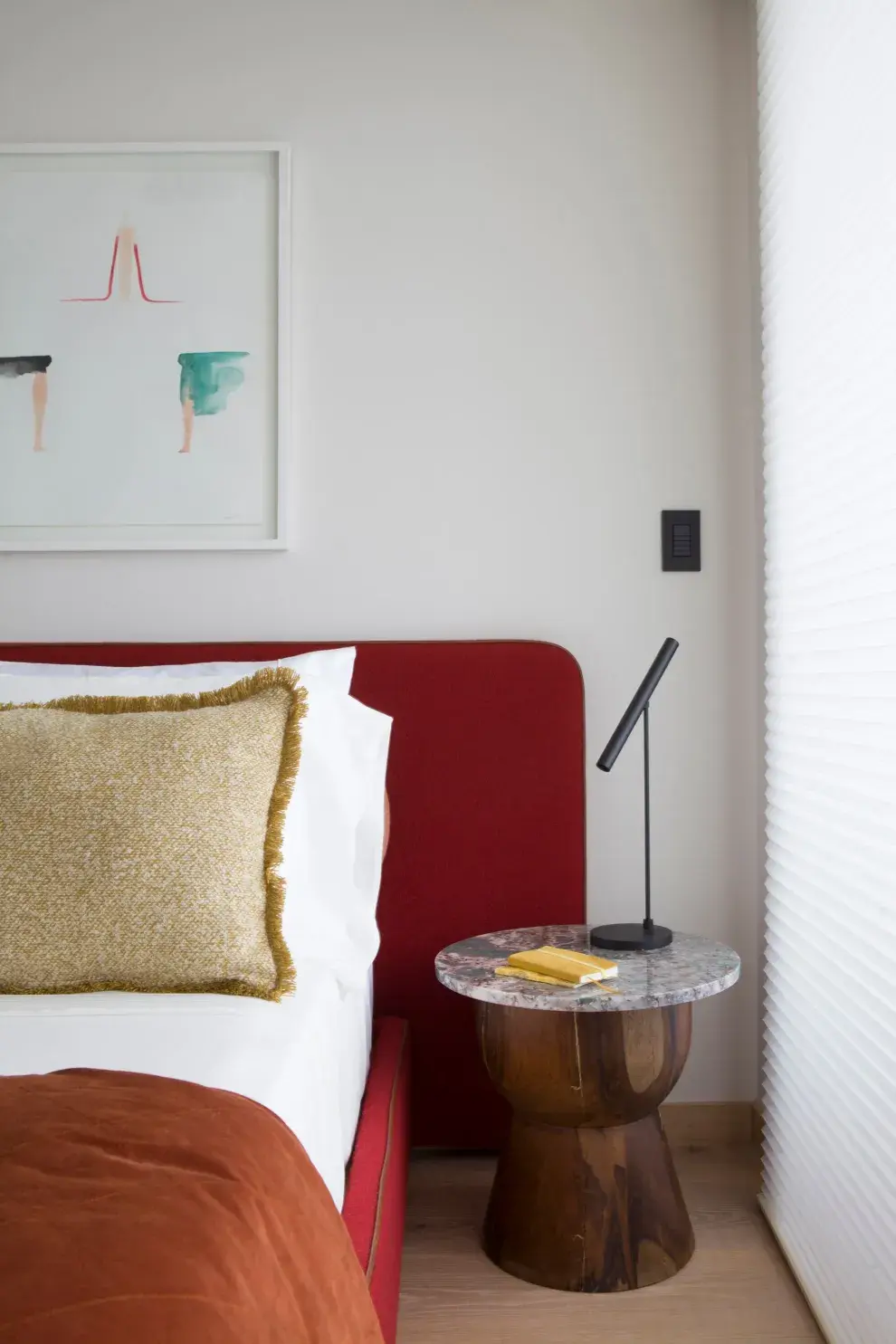 .La lámpara "Wipi" de Idea "simboliza la síntesis pura". Mesa redonda de madera maciza con tapa de mármol veteado. Cama en pana bordó y obra de arte con acuarelas enmarcadas.