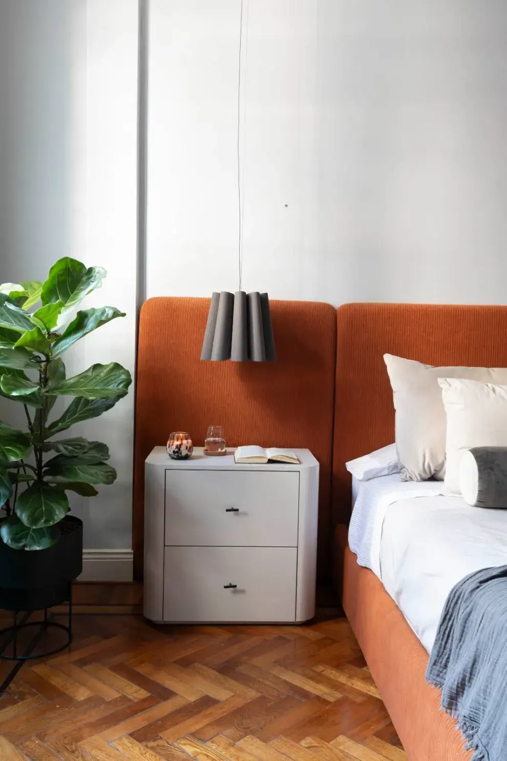 Lámpara colgante ‘Renata 32’ de Iluminación Agüero. Mesa de luz curva y cama con respaldo entelado de Urbano Estudio.