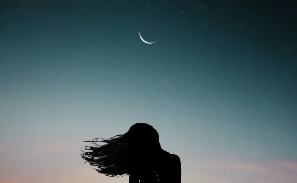 Foto de silueta de mujer observando una luna nueva.