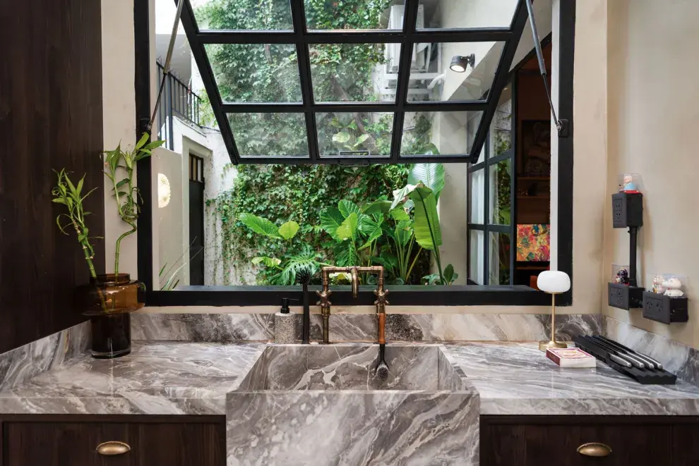 LA MESADA ES DE UN MATERIAL SINTÉTICO ITALIANO QUE SIMULA LA PIEDRA NATURAL. LAS VISTAS DESDE LA COCINA HACIA LA ENREDADERA, UN OASIS EN LA CIUDAD. 