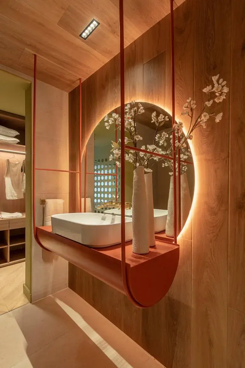 La iluminación deja de ser técnica para volverse protagonista: espejos, paredes y cielos rasos construyen atmósferas más cálidas y envolventes.