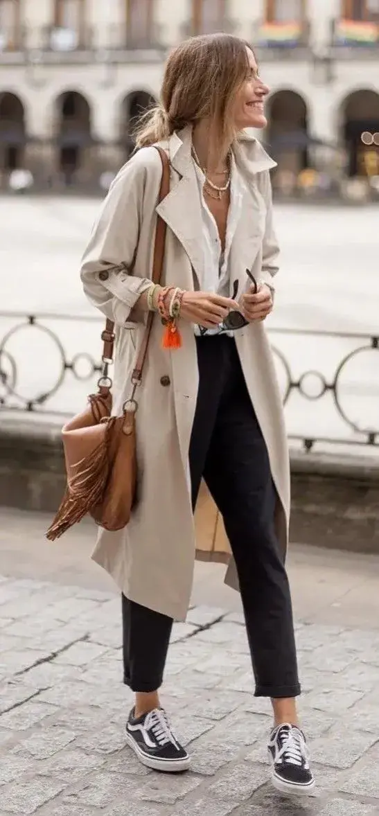 Un trench beige clásico combinado con jean recto azul y camisa blanca logra un look elegante, limpio y muy parisino.