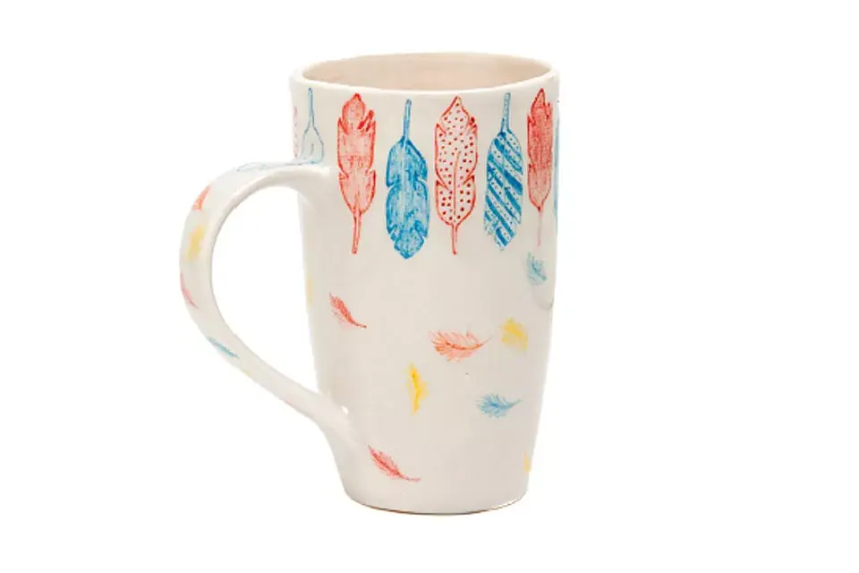 Taza artesanal de cerámica con plumitas pintadas (Maru Decó, $95)