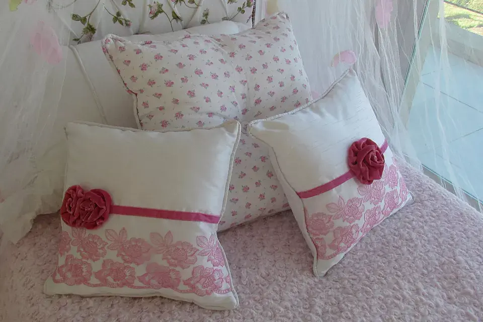 Románticos almohadones con apliques de flores en dos tonos de rosa; detrás, uno estampado y otro en blanco puro (desde $280, Antique Nouveau)