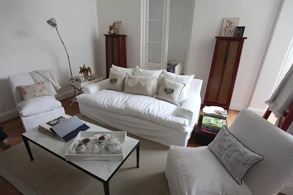El living se armó con un sillón de cuerina con funda de bull blanca, dos silloncitos de herencia familiar, una mesa ratona restaurada con mármol de carrara, una bandeja con patas del mercado de Tigre, un baúl cubiertero regalo de su abuela y dos muebles chinos traídos en un container desde Bruselas