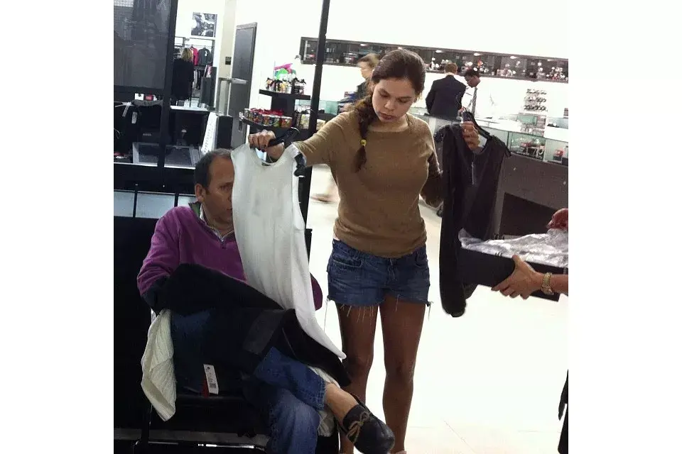 Resignado, este hombre le sostiene las prendas a su mujer sin rechistar