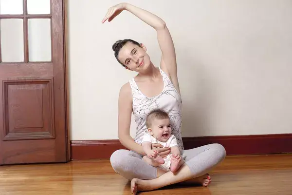 Doblamientos laterales: ahora, sostené a tu bebé con una mano y llevá la otra hacia arriba de tu cabeza sin mover tu cadera; estirate de lado sin perder la línea. 10 repeticiones.