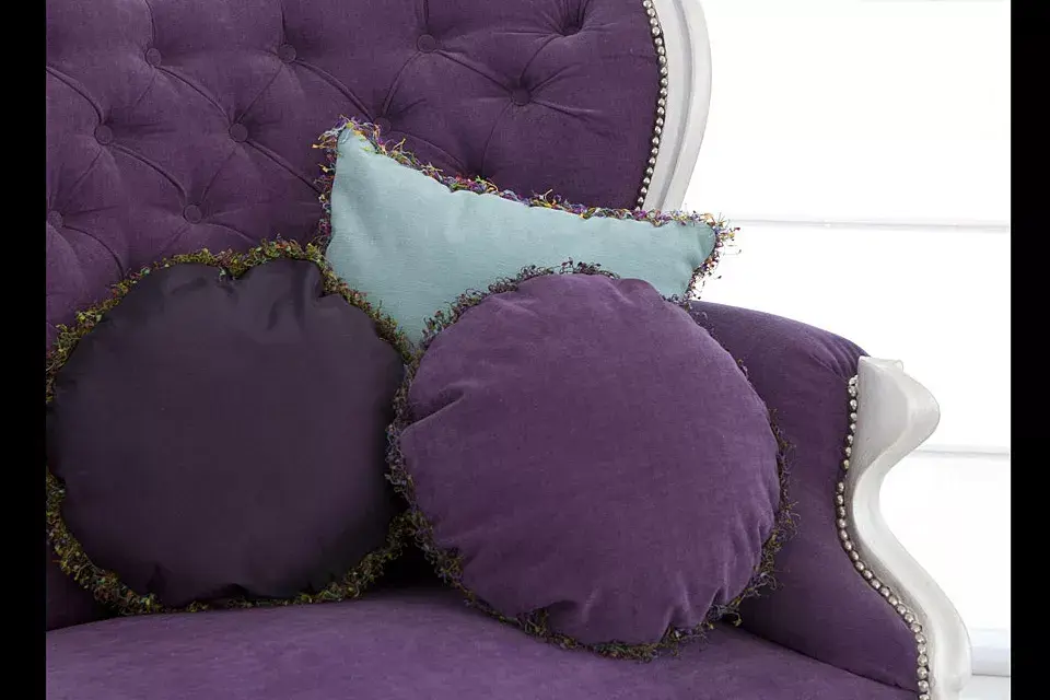 Sobre sillón con respaldo capitoné, almohadones de pana en violeta y lavanda con flecos multicolor (desde $180, Ecléctika)