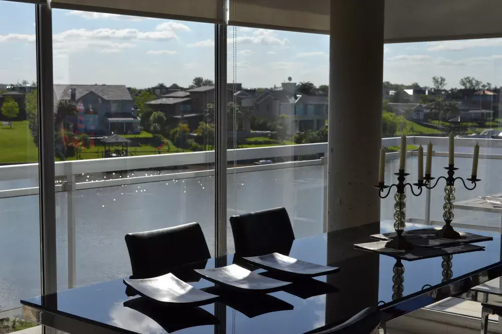 Los grandes ventanales extienden el espacio. En el comedor, la mesa con tapa de cristal Belfast y sillas Chicago ($7485 y $3091, Fontenla). Sobre ella, cuencos de madera y candelabros en vidrio y hierro ($285 c/u, Cuatro Elementos)
