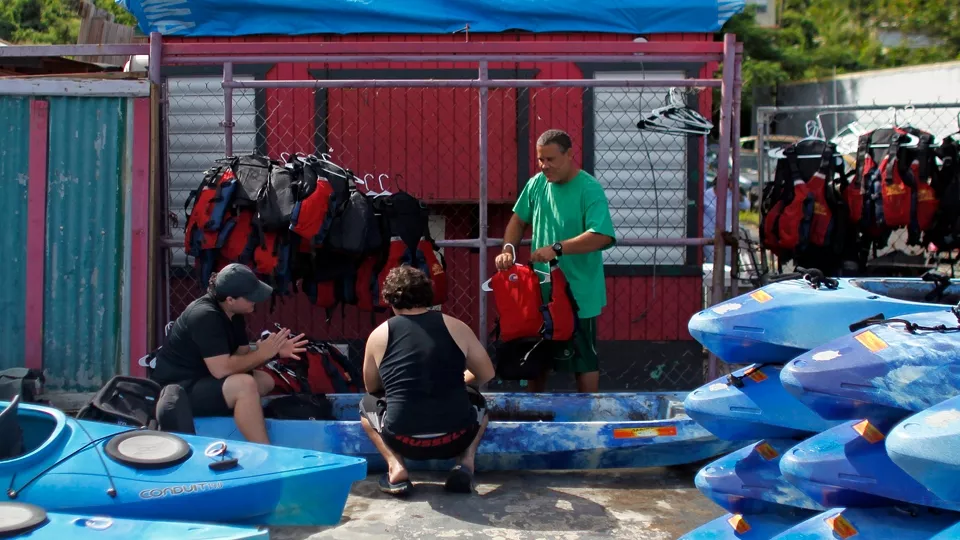 Jose Figueroa (derecha) limpia kayaks con la ayuda de dos compañeros, en la bahía Fajardo, en Puerto Rico