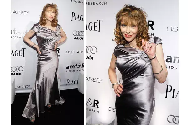 Courtney Love luce muy poco su vestido de seda color gris plata con falda largo con godets y roseta en el escote asimétrico