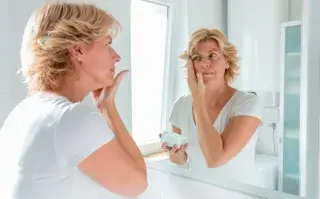Una mujer mirándose al espejo mientras se aplica una crema